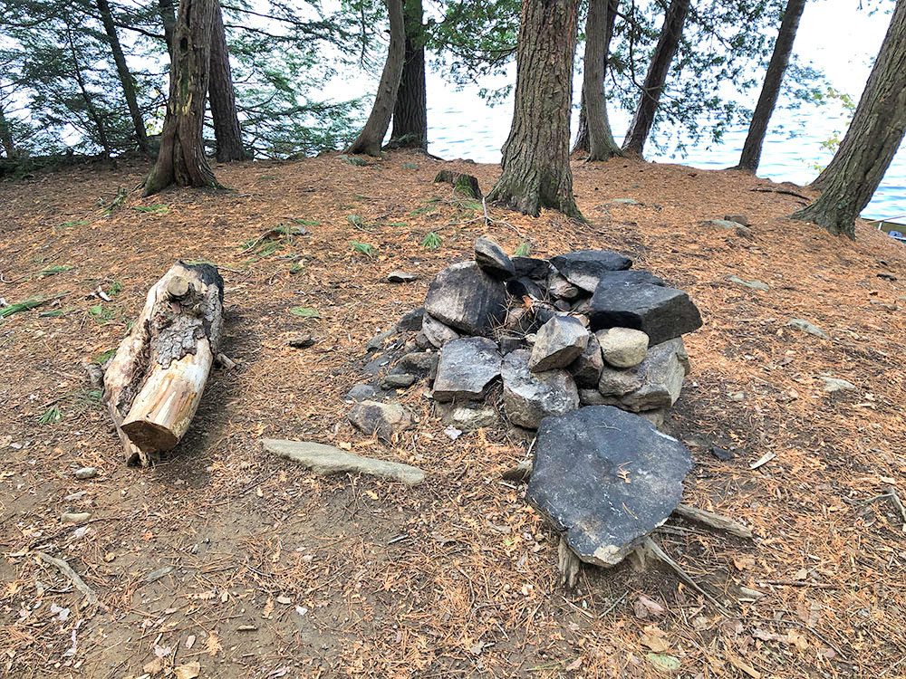 Fire pit with one small log for seating on Ragged Lake campsite #10 in Algonquin Park