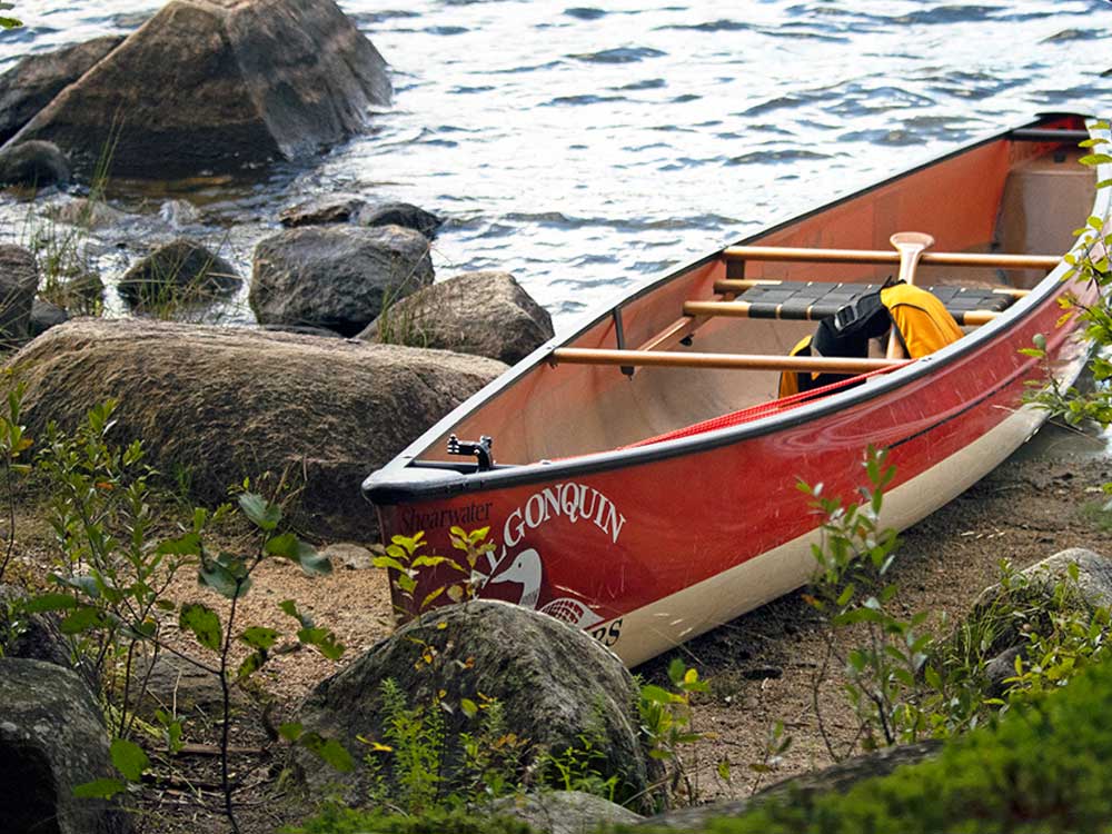 Renting Canoes in Algonquin Park - Red solo canoe at rocky landing at the front of a campsite in Algonquin Park