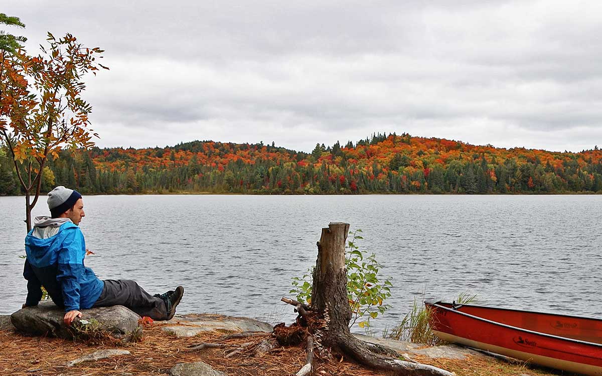 Solo Canoe Trip Tips - sitting solo by the shoreline with fall colours and red canoe