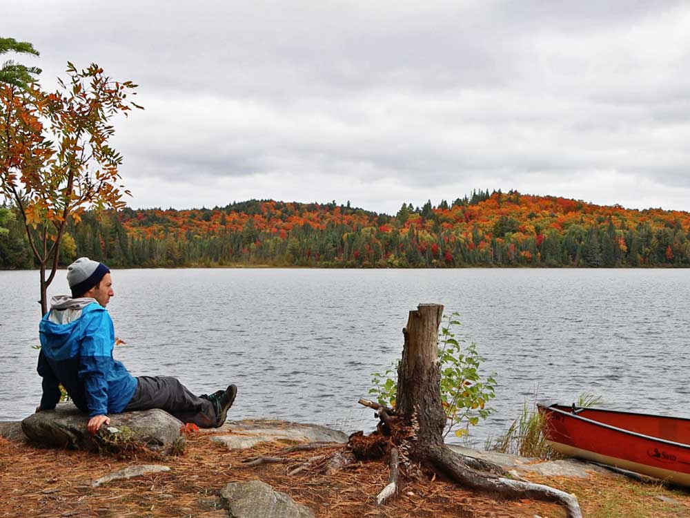 Solo Canoe Trip Tips - Sitting alone by the water with fall shoreline and red canoe